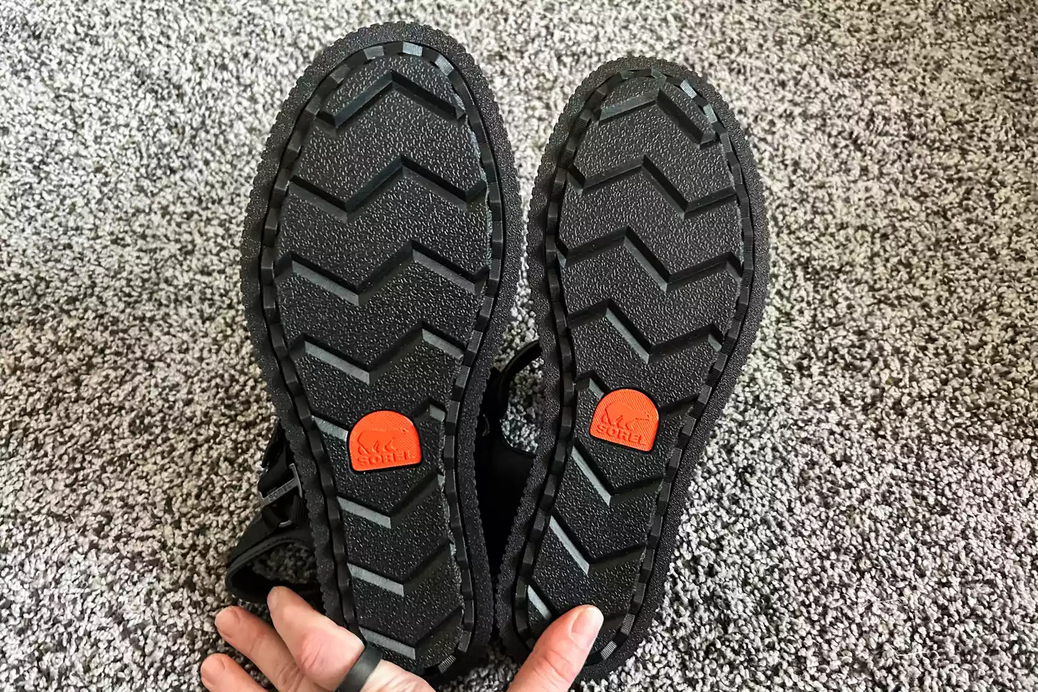 A hand showing the bottom of the Sorel ONA AVE Women's Ankle Strap Flat Sandals on carpet