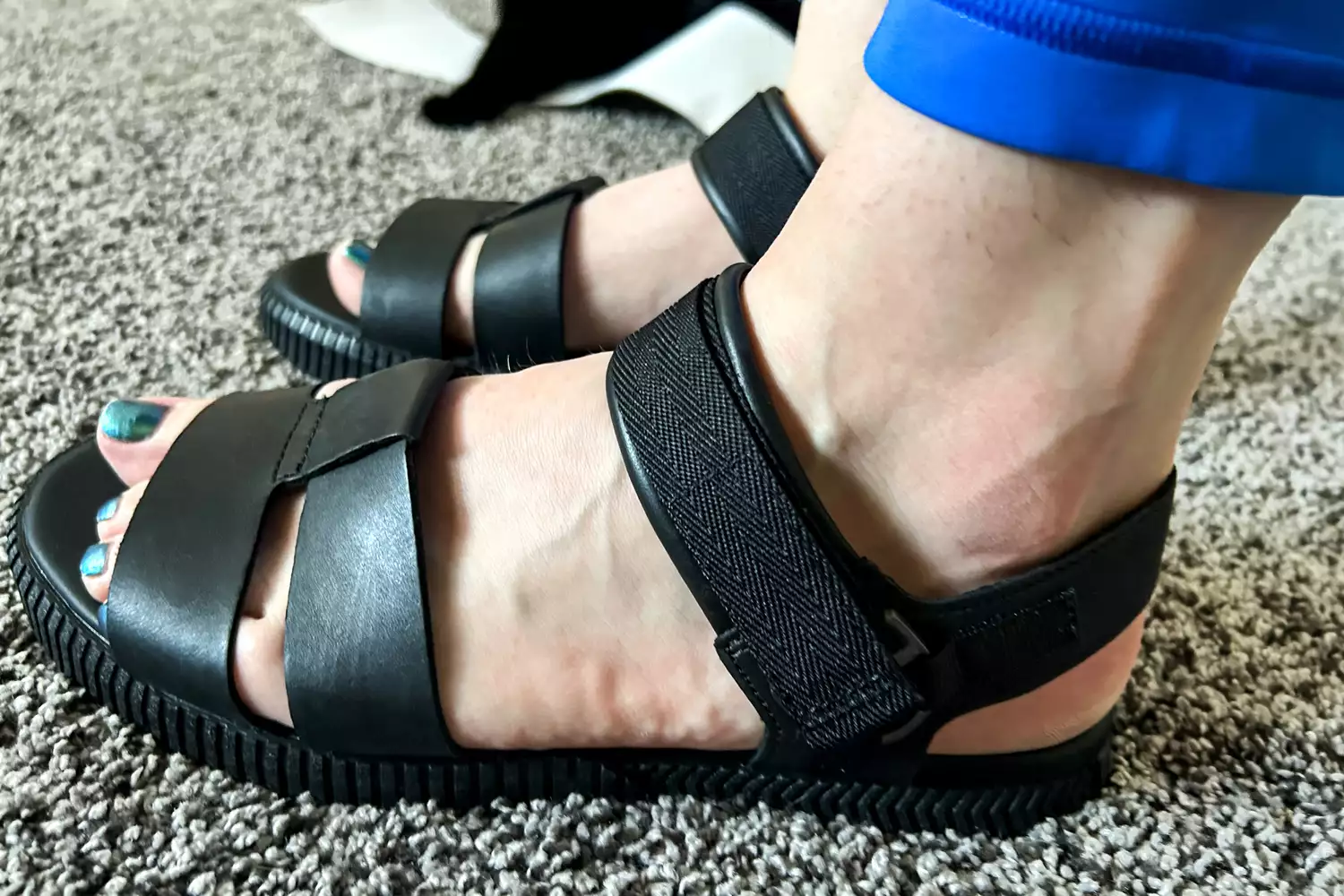 The side view of the Sorel ONA AVE Women's Ankle Strap Flat Sandals worn on carpet