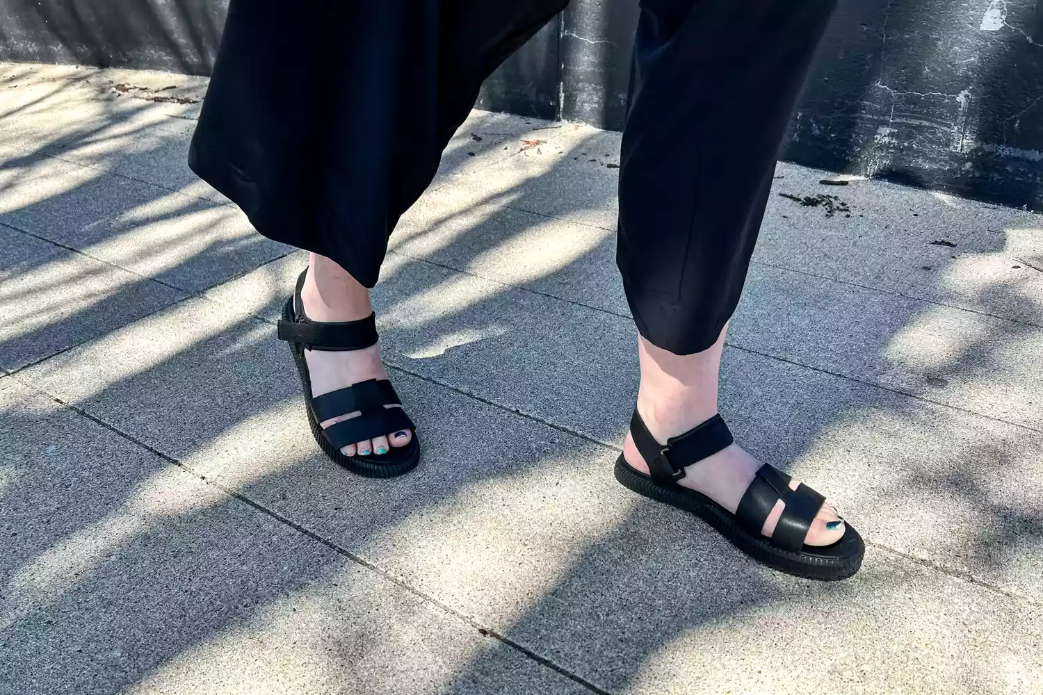 A close-up of feet walking on concrete in the Sorel ONA AVE Women's Ankle Strap Flat Sandal