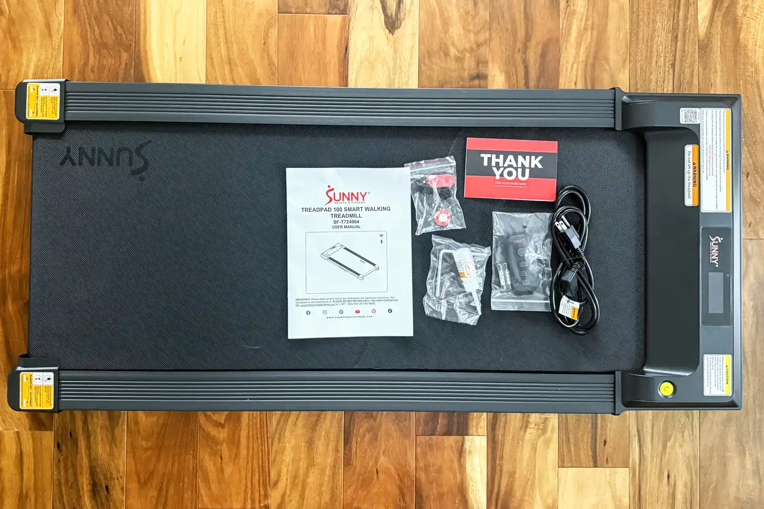 The user manual and accessories on top of the Sunny Health & Fitness Treadpad 100 Smart Wi-Fi Connected Treadmill