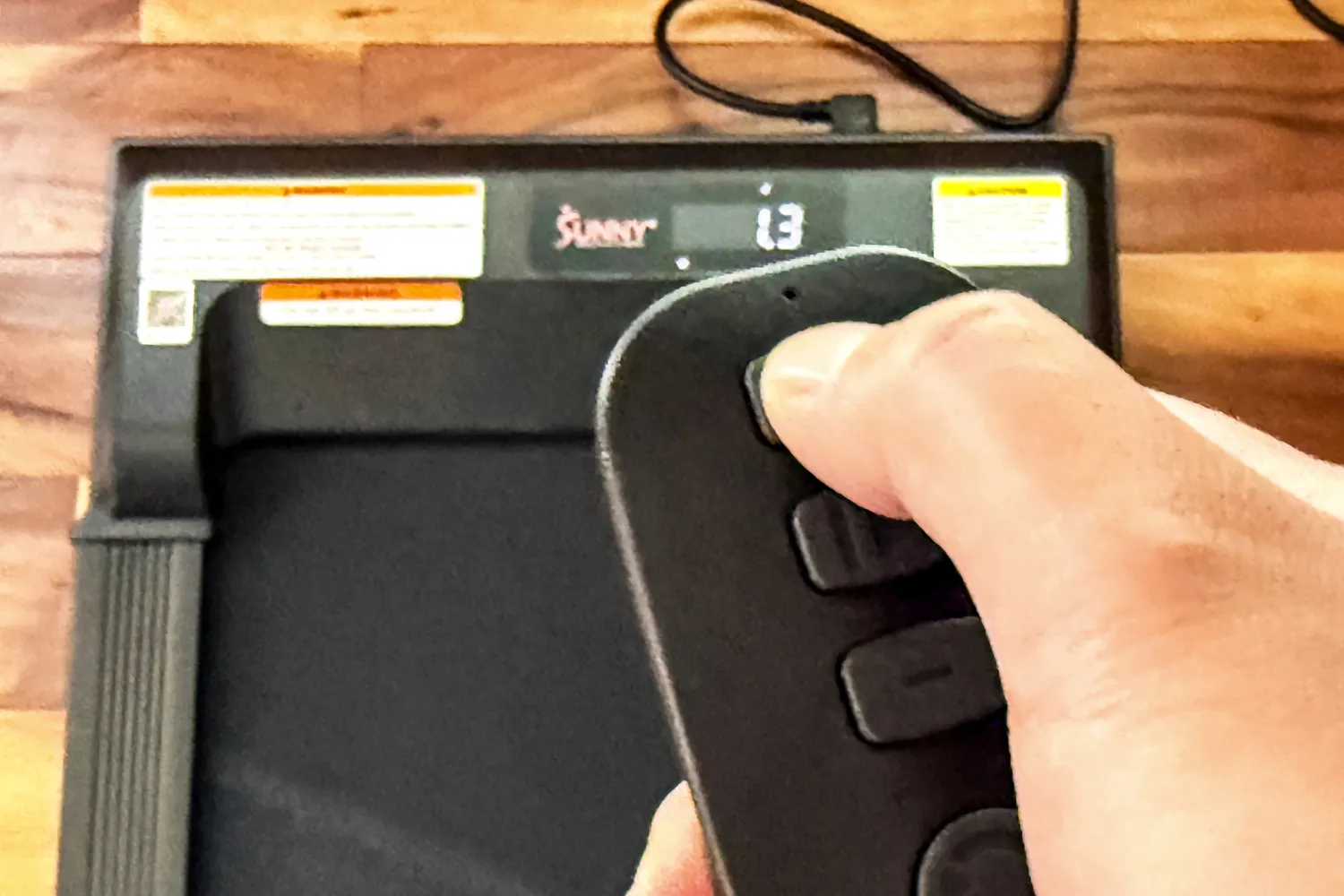 A person presses a button on the Sunny Health & Fitness Treadpad 100 Smart Wi-Fi Connected Treadmill remote control