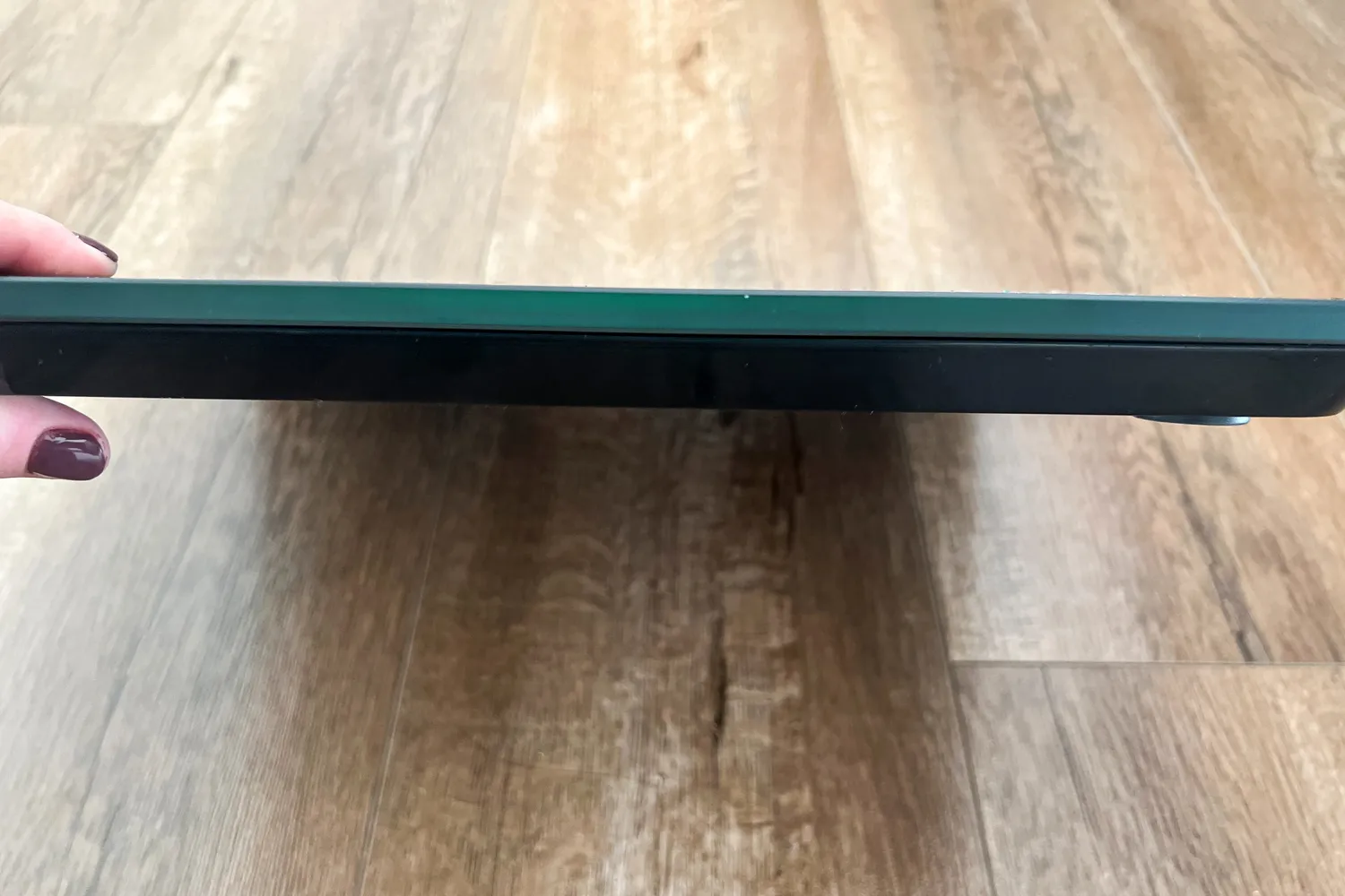 A person lifts the Tanita HD-384 Digital Bathroom Scale to show the thickness of it