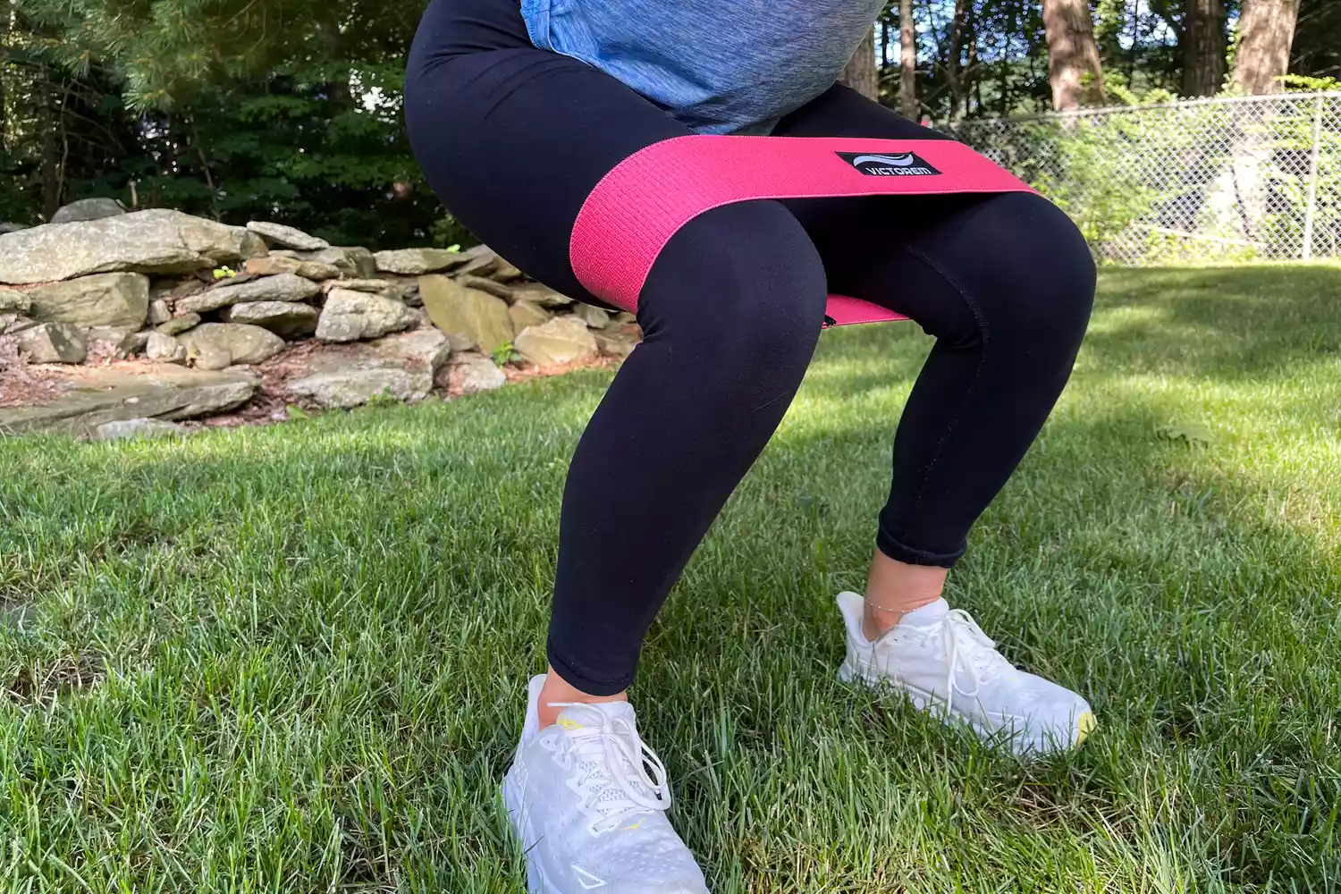 A close-up of a person doing a squat on grass with the red Victorem Resistance Hip Booty Band