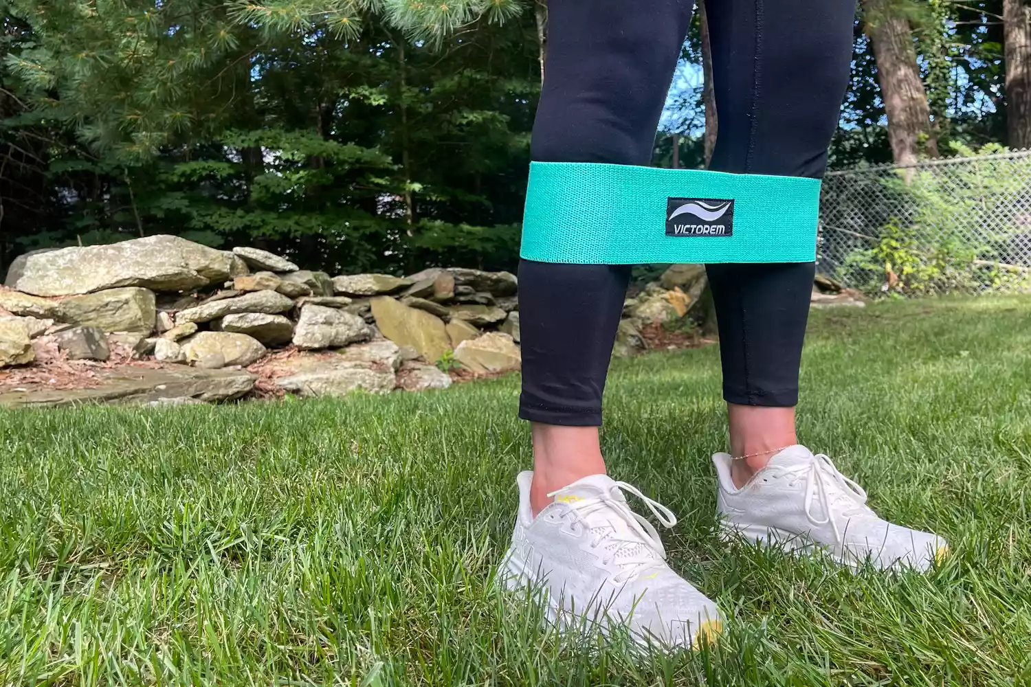 A close-up of the knees down of a person wearing the teal Victorem Resistance Hip Booty Band on their calf