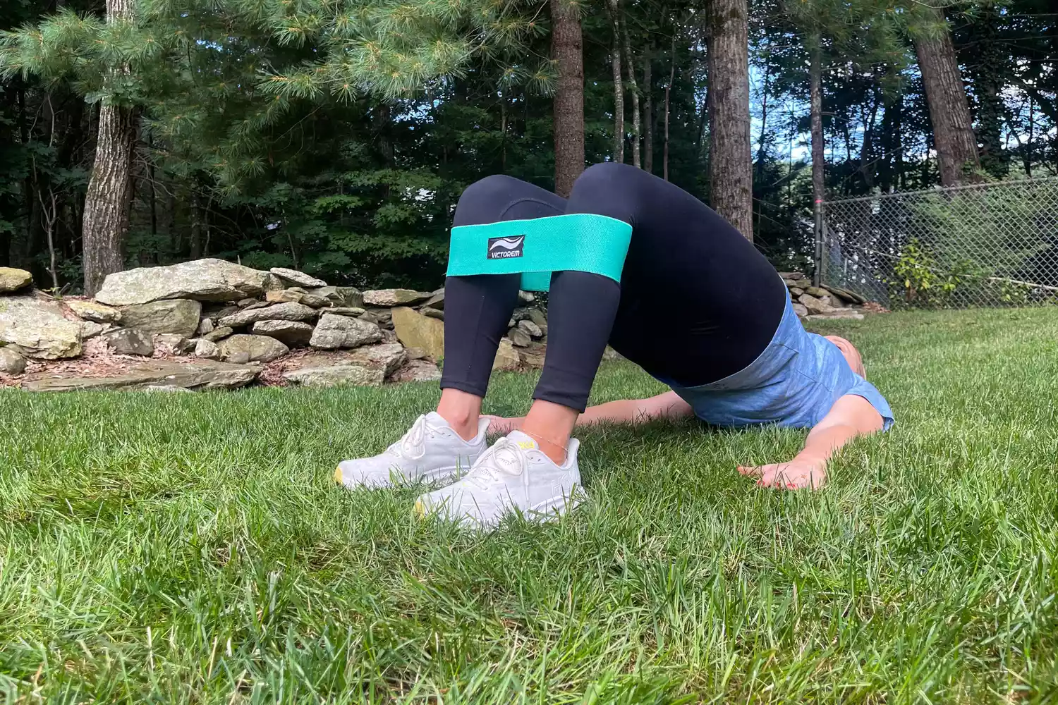 A person doing bridge on grass while wearing a teal Victorem Resistance Hip Booty Band on their calfs