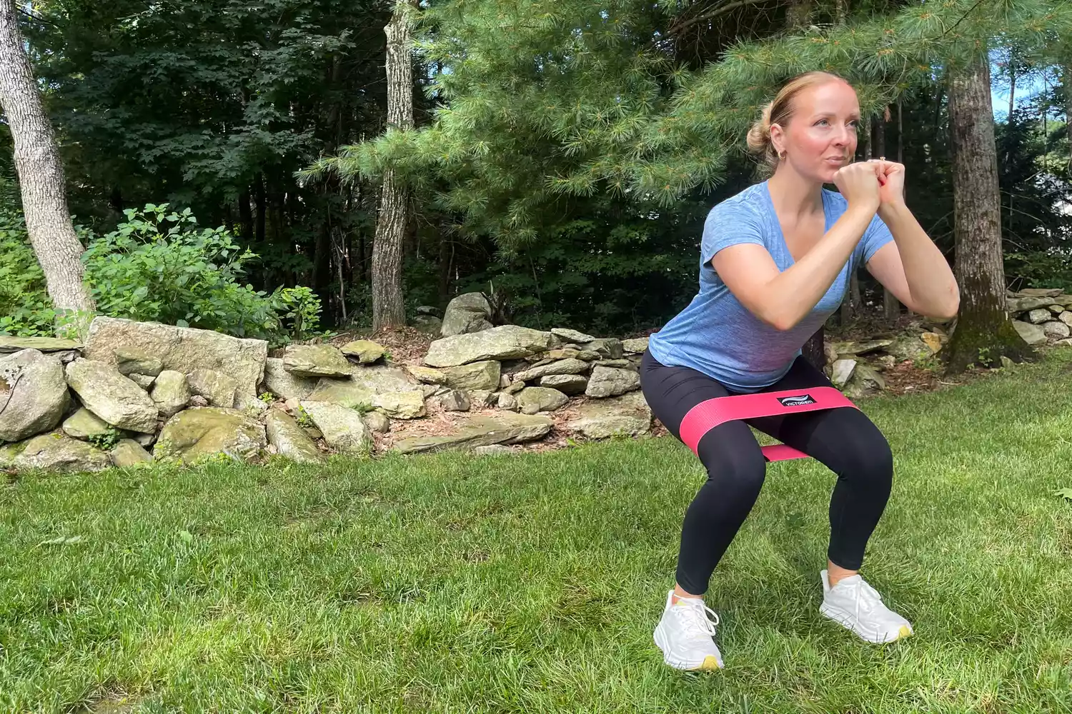 A person doing a squat while wearing the red Victorem Resistance Hip Booty Band outdoors on grass