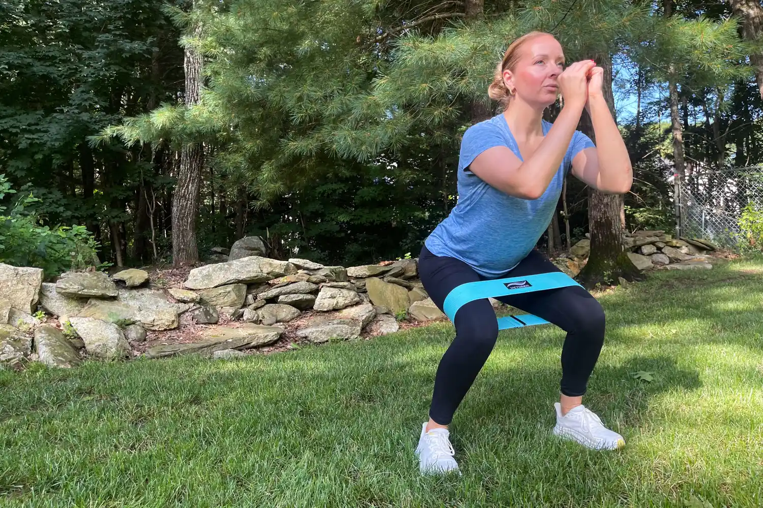 A person using a resistance band around their thighs while performing a squat in an outdoor setting