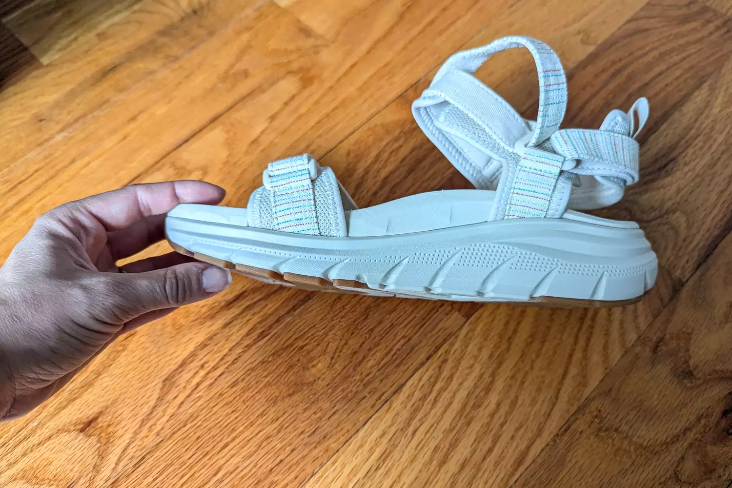 A hand showing the side of a Vionic Walk Max Wanderer Sandal on a wooden surface