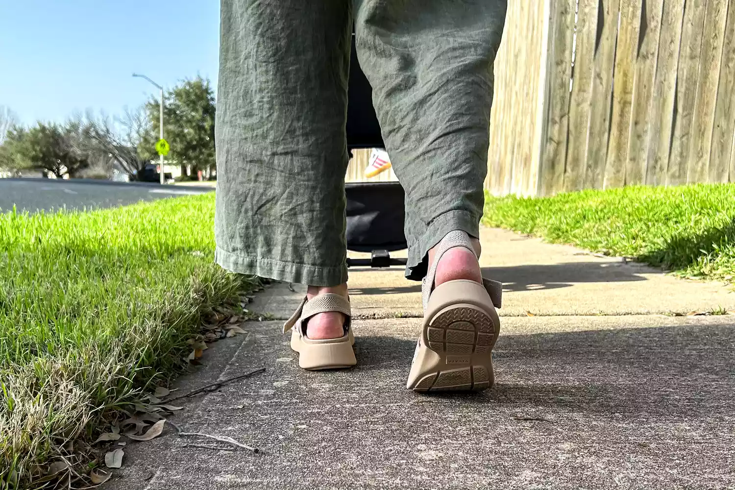 A close-up of a person's legs from the back while walking on the sidewalk wearing the Vivaia Kiara Sport Sandals