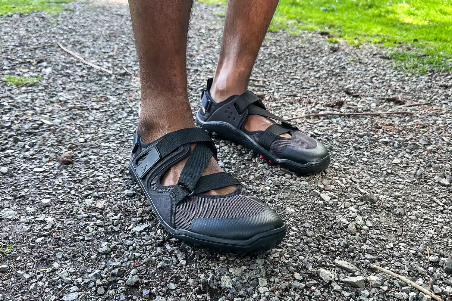 A person wears the Vivobarefoot Men's Tracker Sandals while walking on a rocky trail