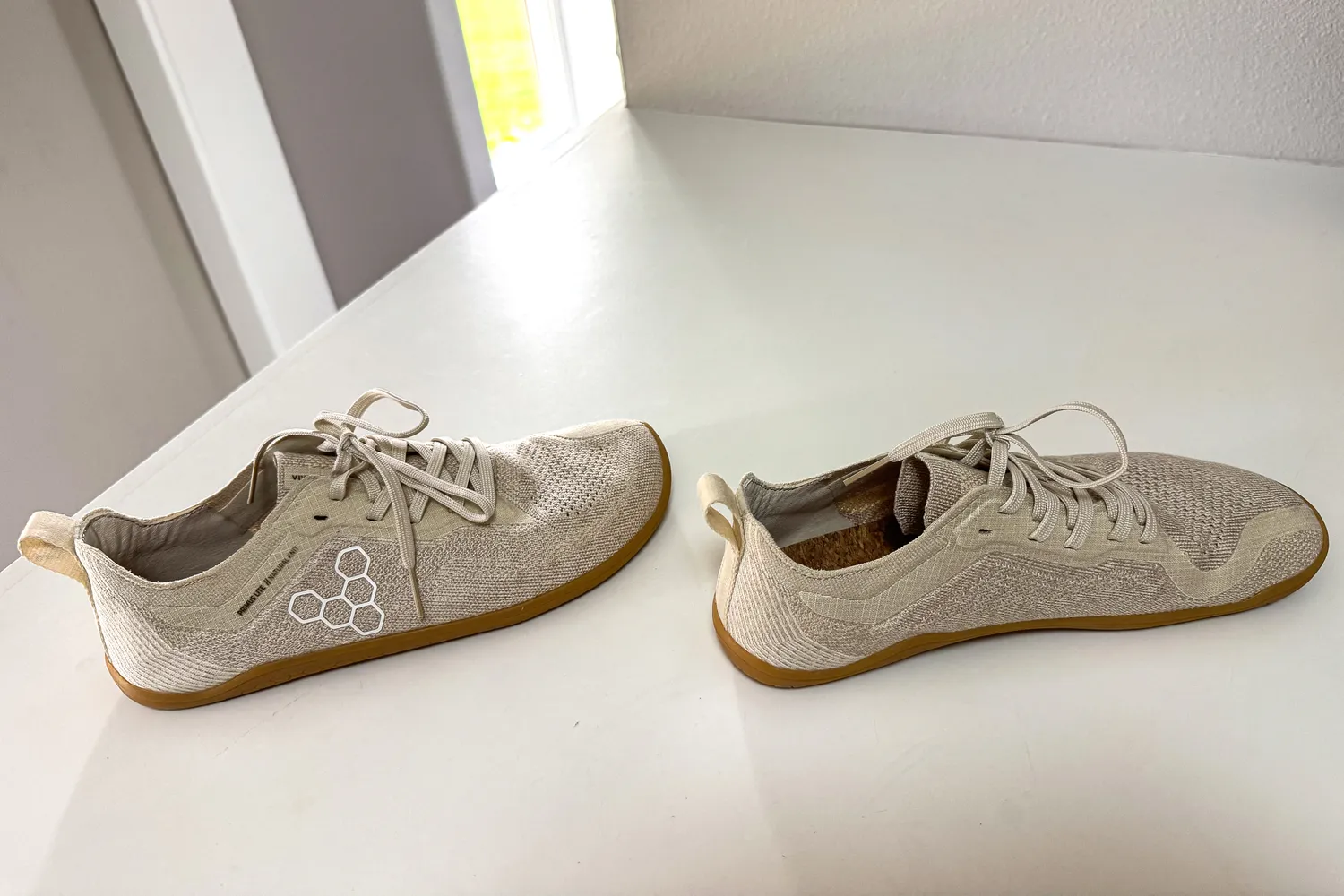 A pair of Vivobarefoot Women's Primus Lite Knit Natural Sneaker on a white table