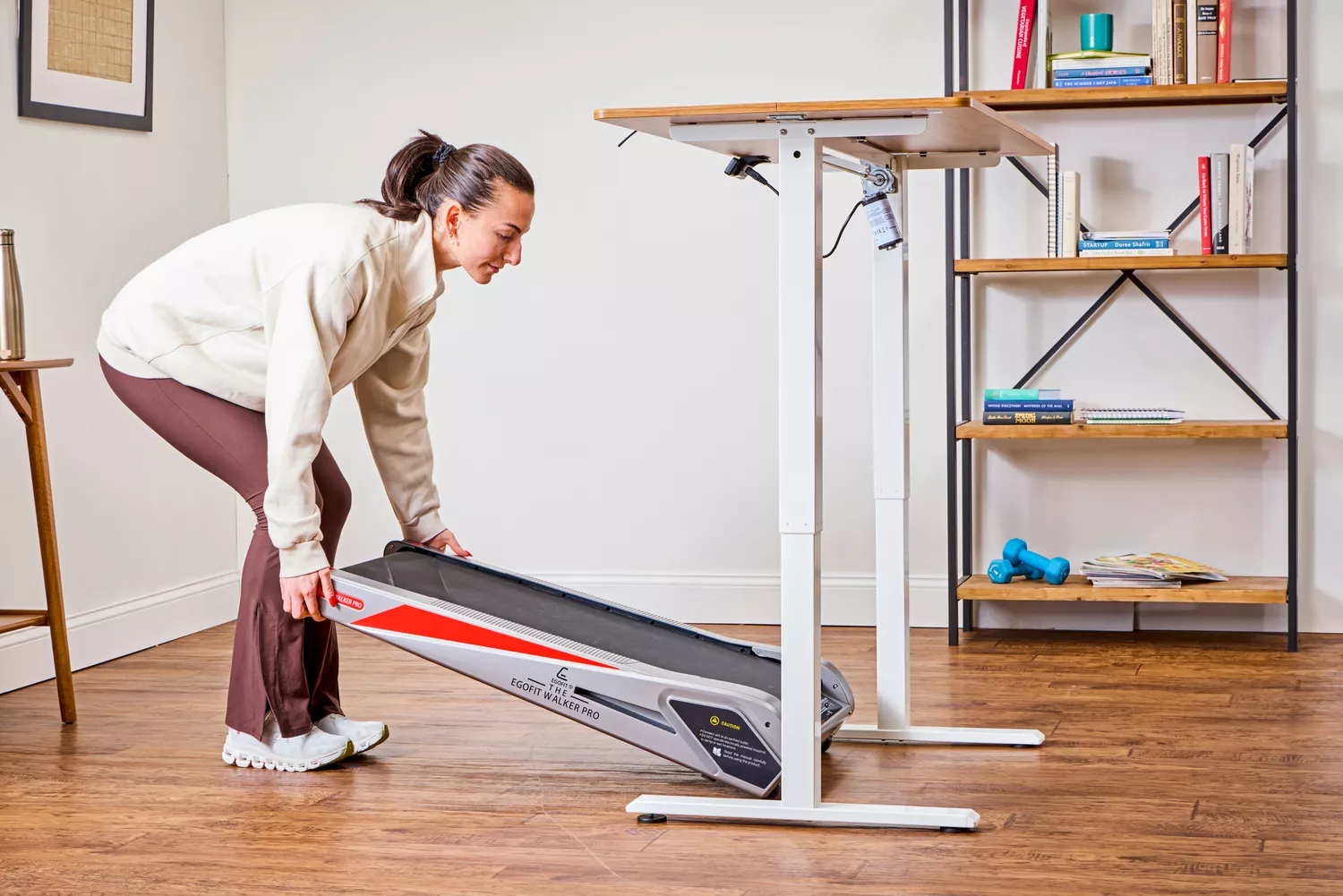 A person placing the Egofit Walker Pro-M1 Treadmill under a desk