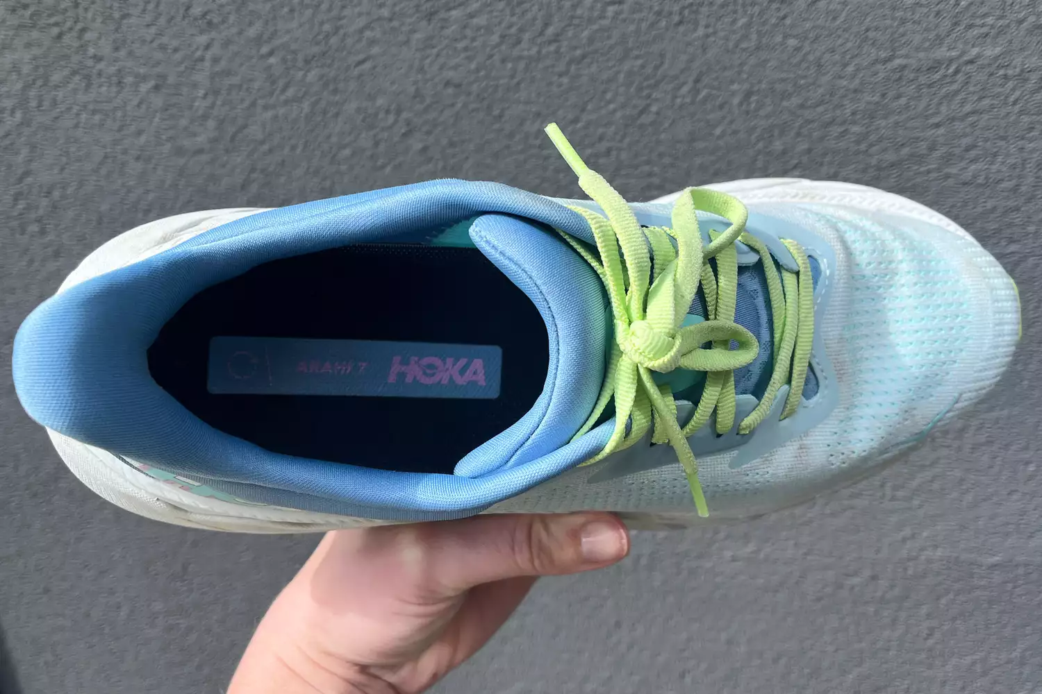A person holds up the Hoka Womenâs Arahi 7 shoe