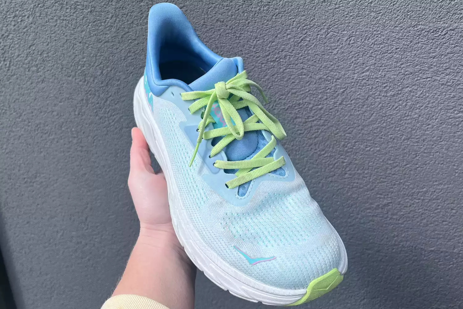 A person holds up the Hoka Womenâs Arahi 7 shoe with the laces tied