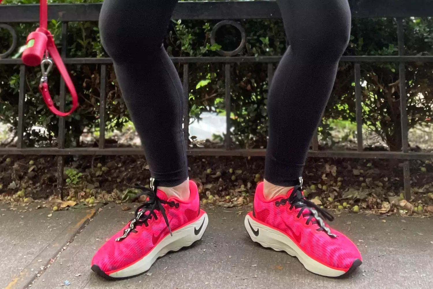Feet wearing Nike Motiva Women's Walking Shoes on sidewalk near fence