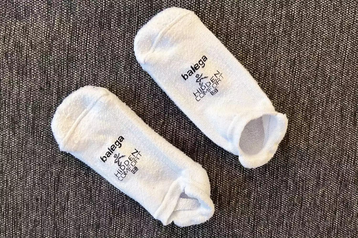 A white pair of Balega Hidden Comfort No-Show Running Socks on a gray cushion