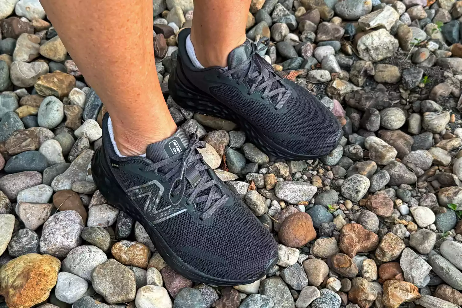 A person wears the New Balance Women's Fresh Foam Arishi v4 GTX Running Shoes while standing on pebbles