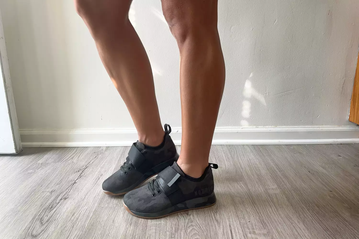 A person stands on a wooden floor while wearing the NOBULL Women's Canvas Lifter Shoe