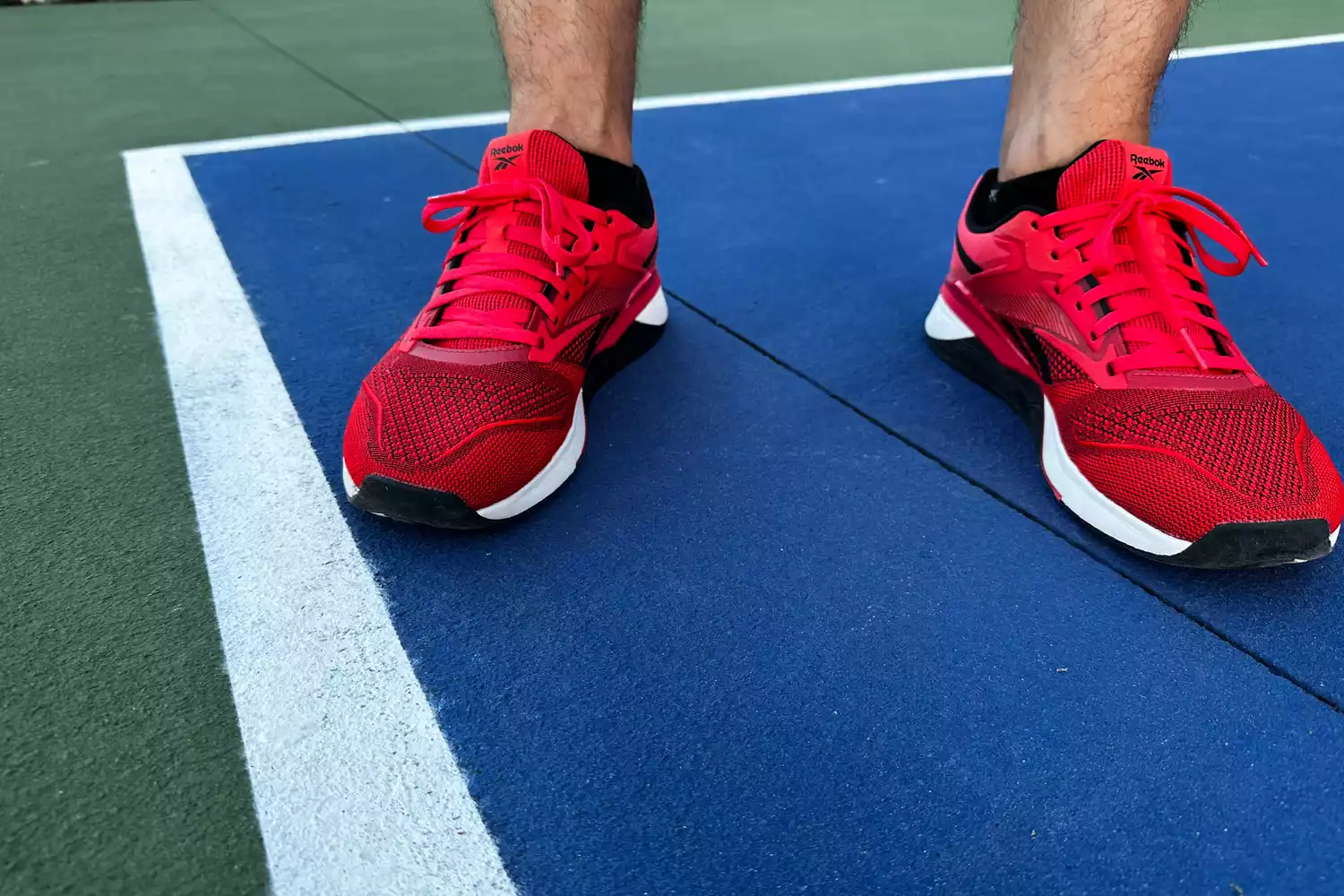 A person stands outside on a court wearing the Reebok Unisex Nano X4 Training Shoes