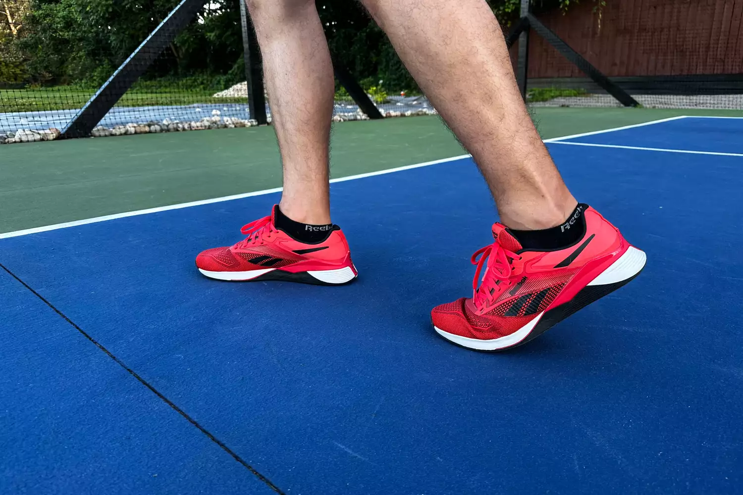 A person walks across an outdoor court while wearing the Reebok Unisex Nano X4 Training Shoes