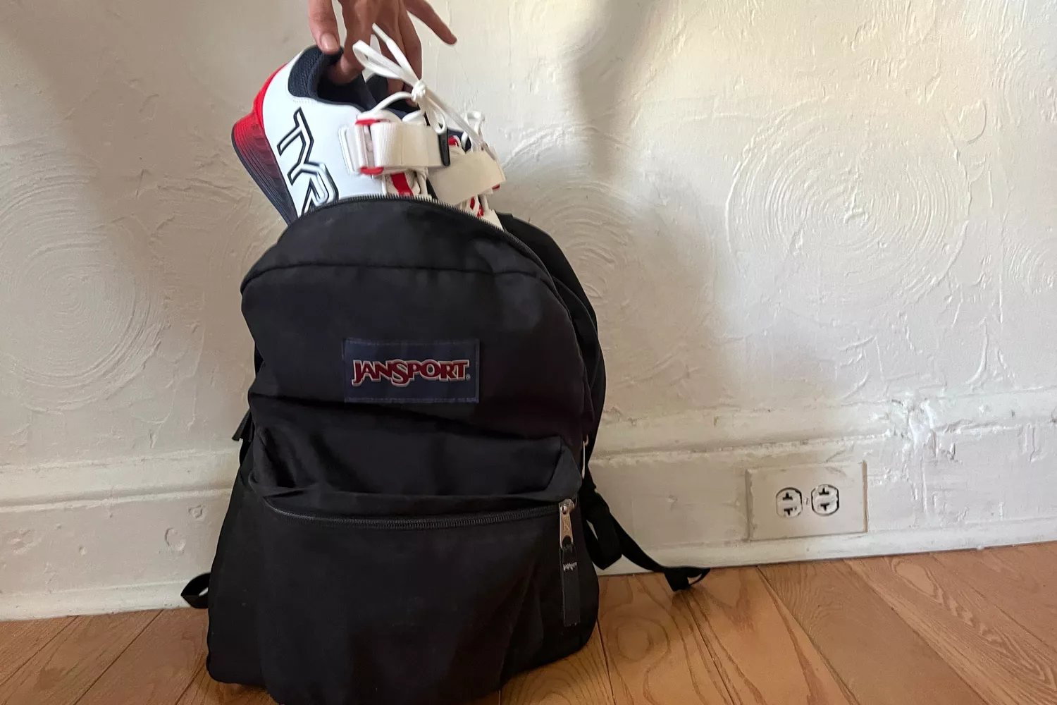 A person places a pair of TYR Women's L-1 Lifter Shoes into a backpack