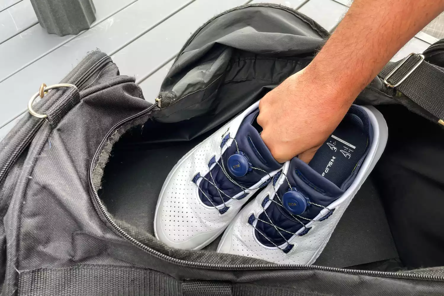 A person places a pair of Under Armour Unisex UA SlipSpeed Training Shoes into a duffel bag