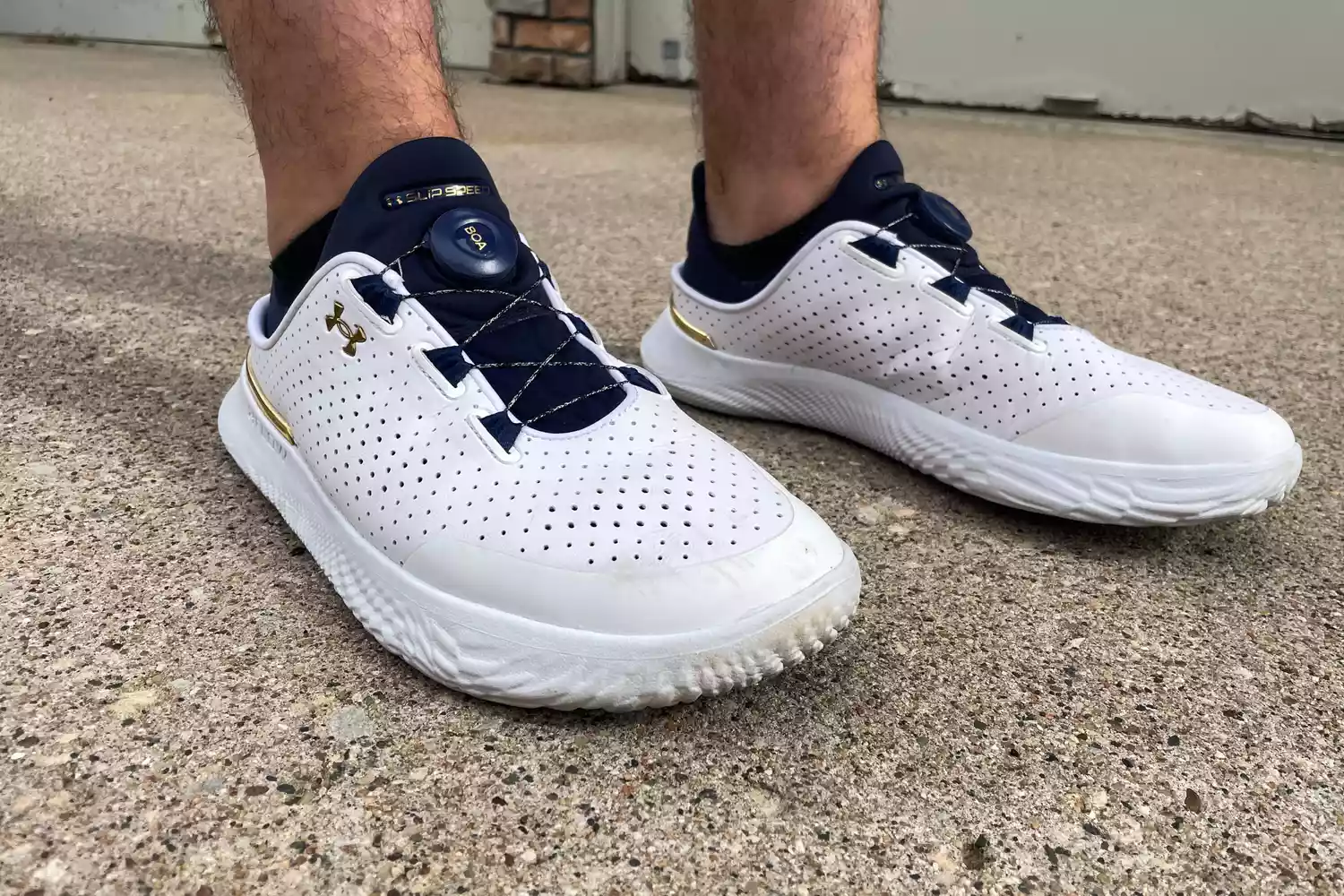 A person stands outside on concrete while wearing the Under Armour Unisex UA SlipSpeed Training Shoes