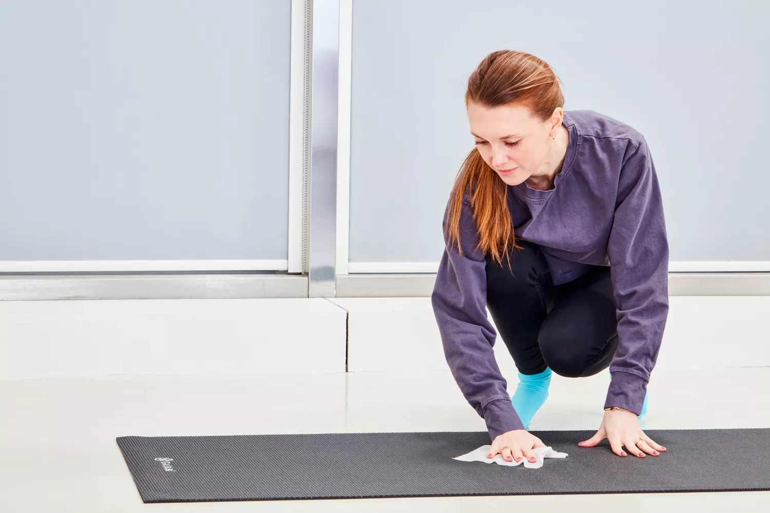 A woman wipes down a Gaiam Classic Solid 5mm Yoga Mat with a cloth