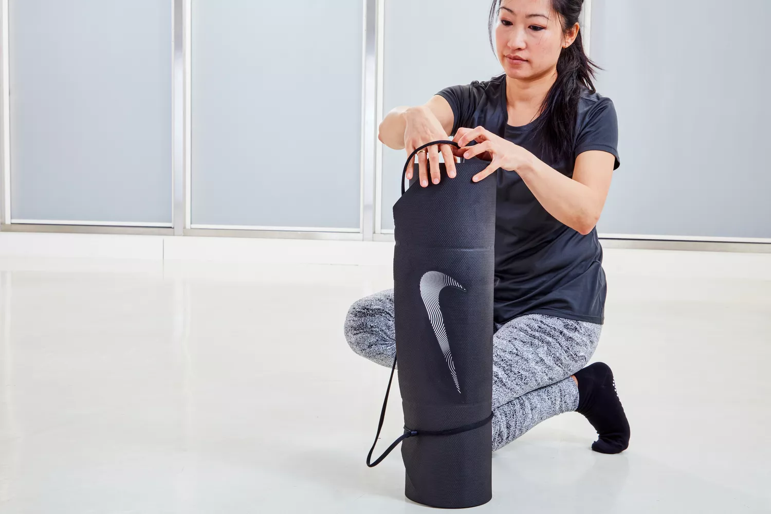 A woman holds a rolled up Nike Training Mat 2.0 vertically