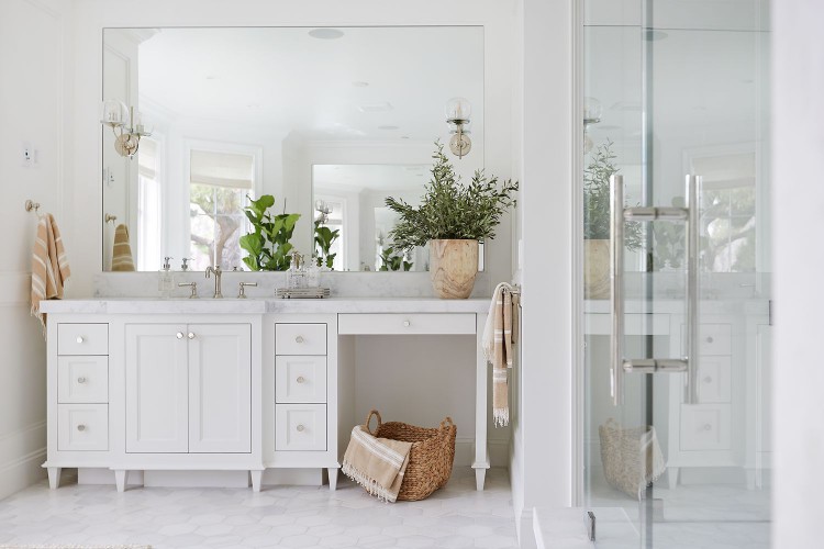 A bathroom that's all-white, aside from a few beige accents and a couple green plants