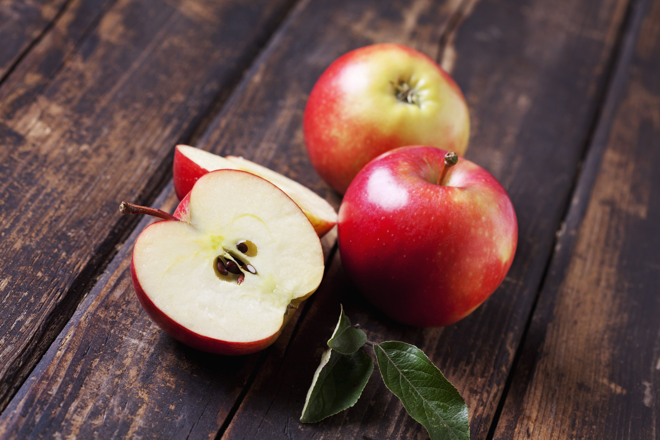 Whole and sliced red apples on dark wood