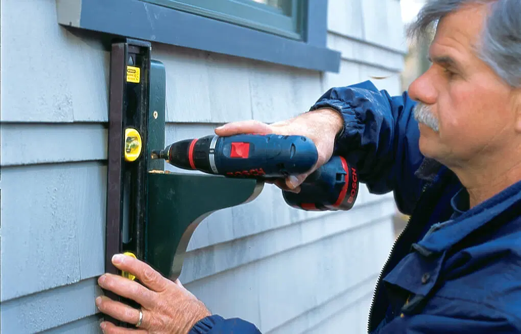 Tom Silva screws in a second screw and measures that the window box bracket is straight.