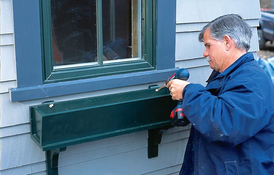 Silva screws the window box on the brackets.