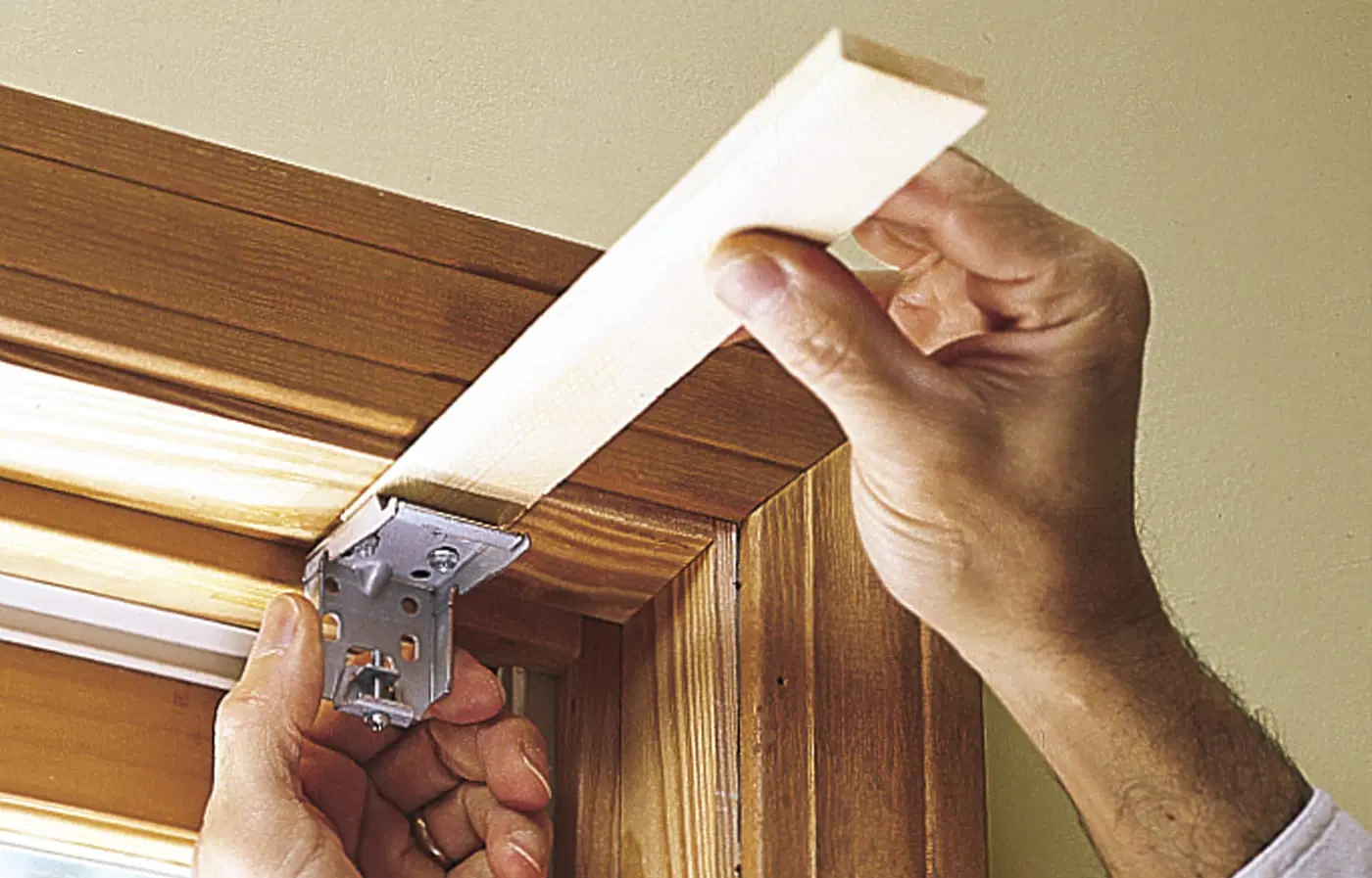 A thin wood shim being placed into a mounting bracket for window shades.