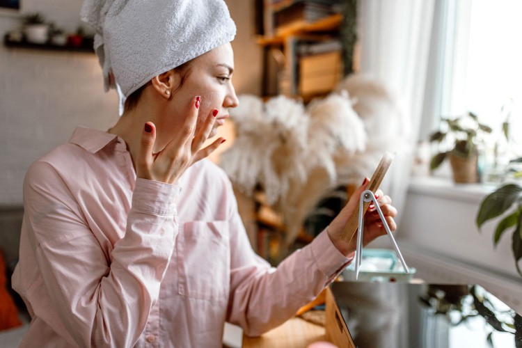 woman applying skincare while holding mirror