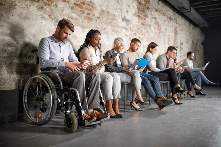 Job seekers sit in a row of chairs, waiting for an interview.