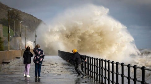 People walking in Folkestone while waves created by Storm Ciar谩n crash into the promenade