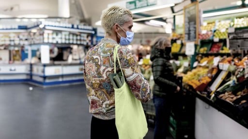 person with floral print blouse, short bleached hair, and face mask shopping for food in a supermarket
