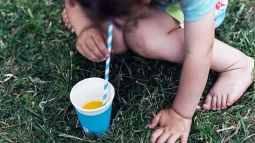 Close up of a child drinking orange juice from a disposable cup with a straw on grass outside