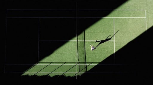 An aerial shot of tennis match from above with the player's shadow reflecting onto the court