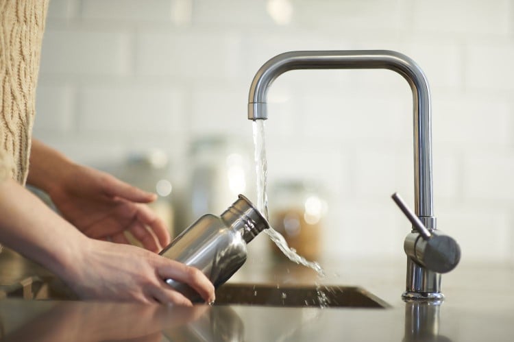 woman cleans reusable water bottle in sink